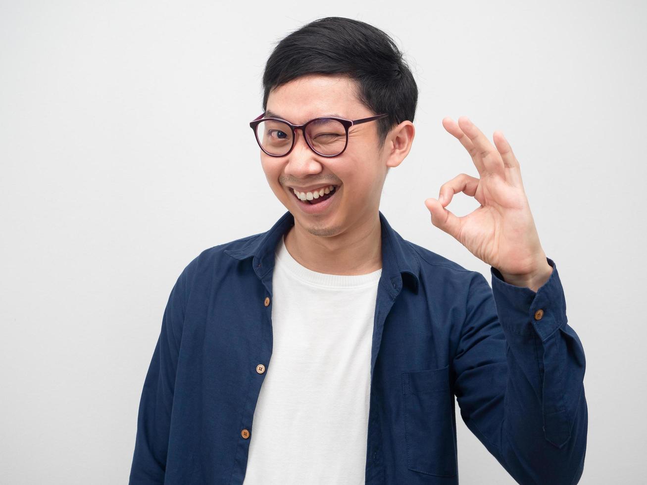 homem alegre de óculos fecha o olho e faz a mão ok sorriso feliz foto