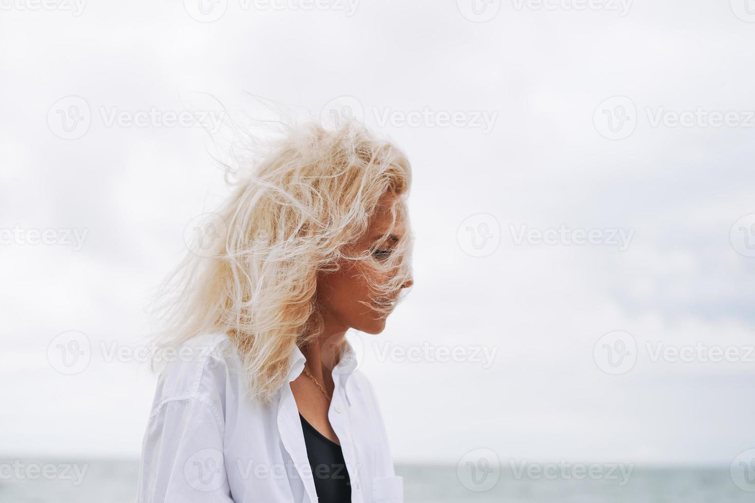 retrato de mulher loira elegante na camisa branca na praia de areia no mar de tempestade no tempo ventoso foto