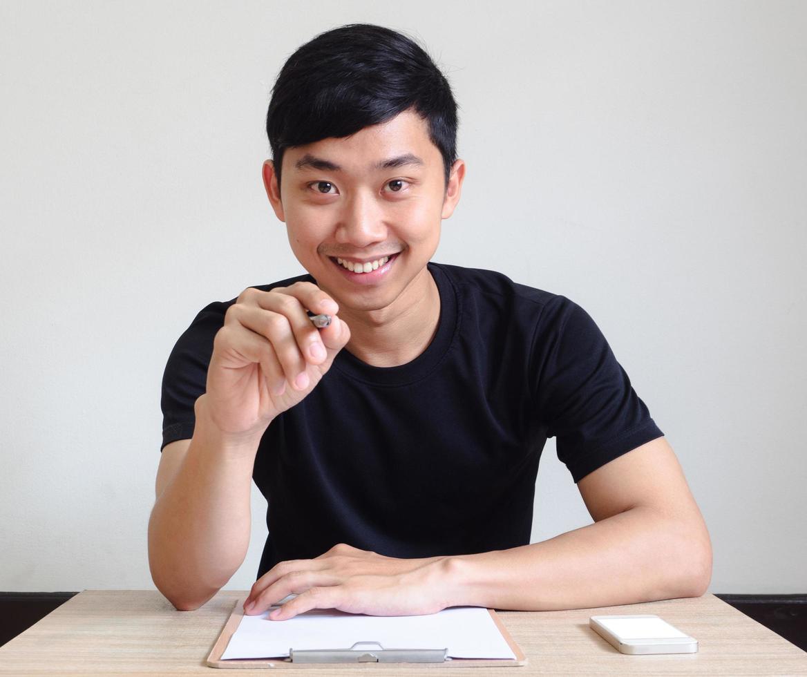 homem, sorriso feliz, sente-se na mesa, aponte a caneta para você, o conceito de entrevista foto