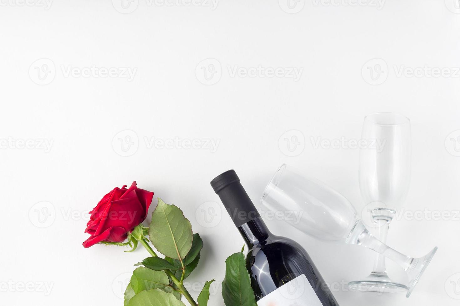 garrafa de vinho, vidro e rosa vermelha com pétalas em um fundo branco foto