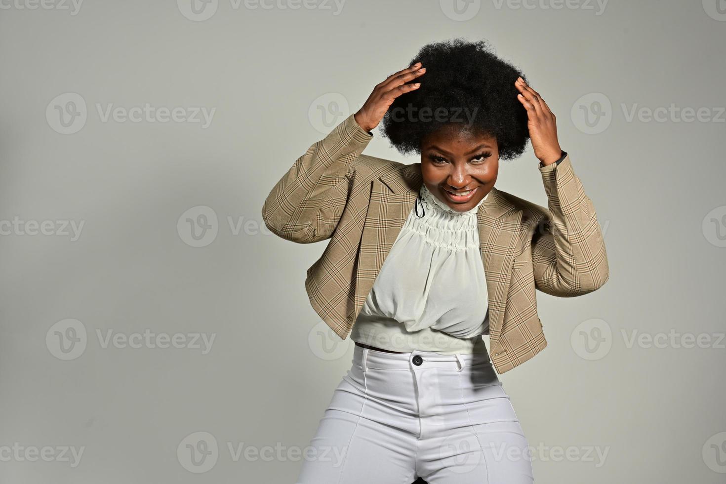linda mulher afro-americana com acessórios da moda e penteado afro, olhando para a câmera contra um fundo cinza foto