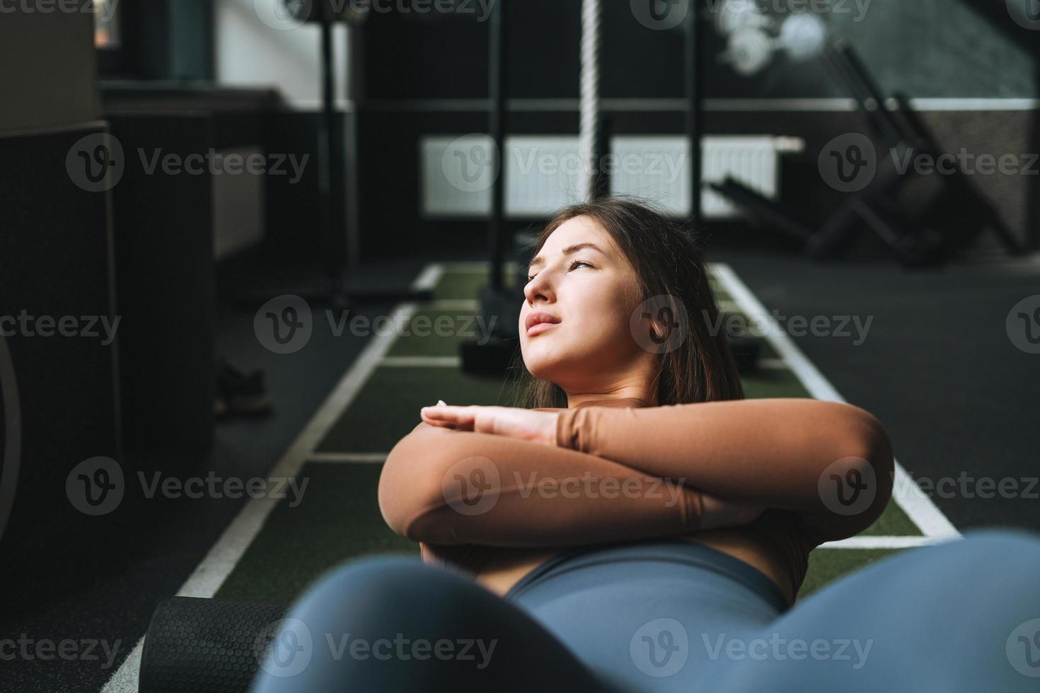 jovem morena fazendo alongamento pilates, pratica ioga em rolo no clube de fitness foto