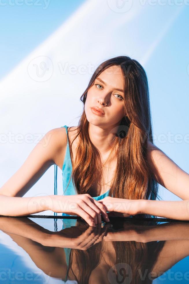 retrato da beleza com água de modelo de moda jovem com cabelo longo escuro saudável sobre fundo azul foto