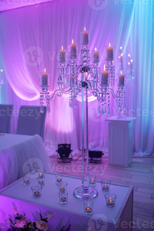 mesa festiva decorada com composição de velas e castiçais de prata em luz colorida no salão de banquetes. mesa recém-casados na área de banquetes na festa de casamento. foto
