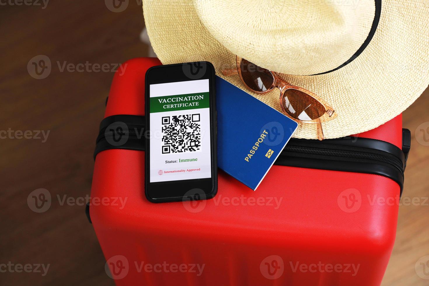 novo conceito normal. close-up vista de um smartphone com um passaporte de saúde digital imune, uma mala vermelha, máscara protetora, chapéu de palha, passaporte e óculos de sol. viajar de avião durante uma pandemia. foto