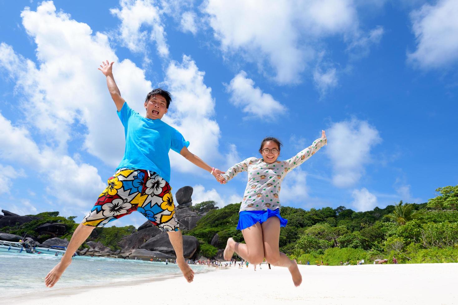 pai e filha pulando na praia na tailândia foto