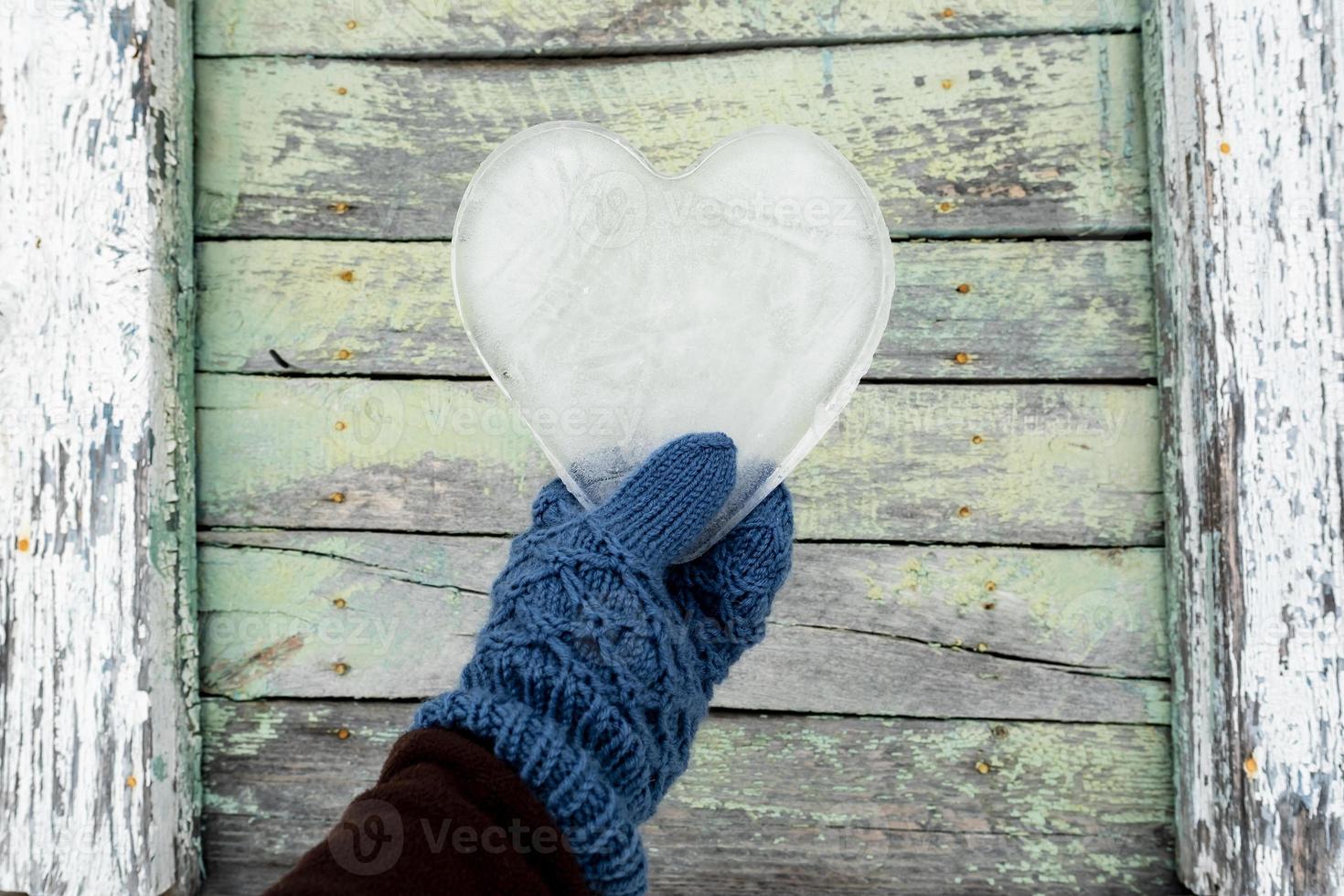 Dia dos Namorados. coração, um símbolo do amor, feito de gelo, é segurado por uma mão em luvas contra o fundo de uma velha parede de madeira. foto