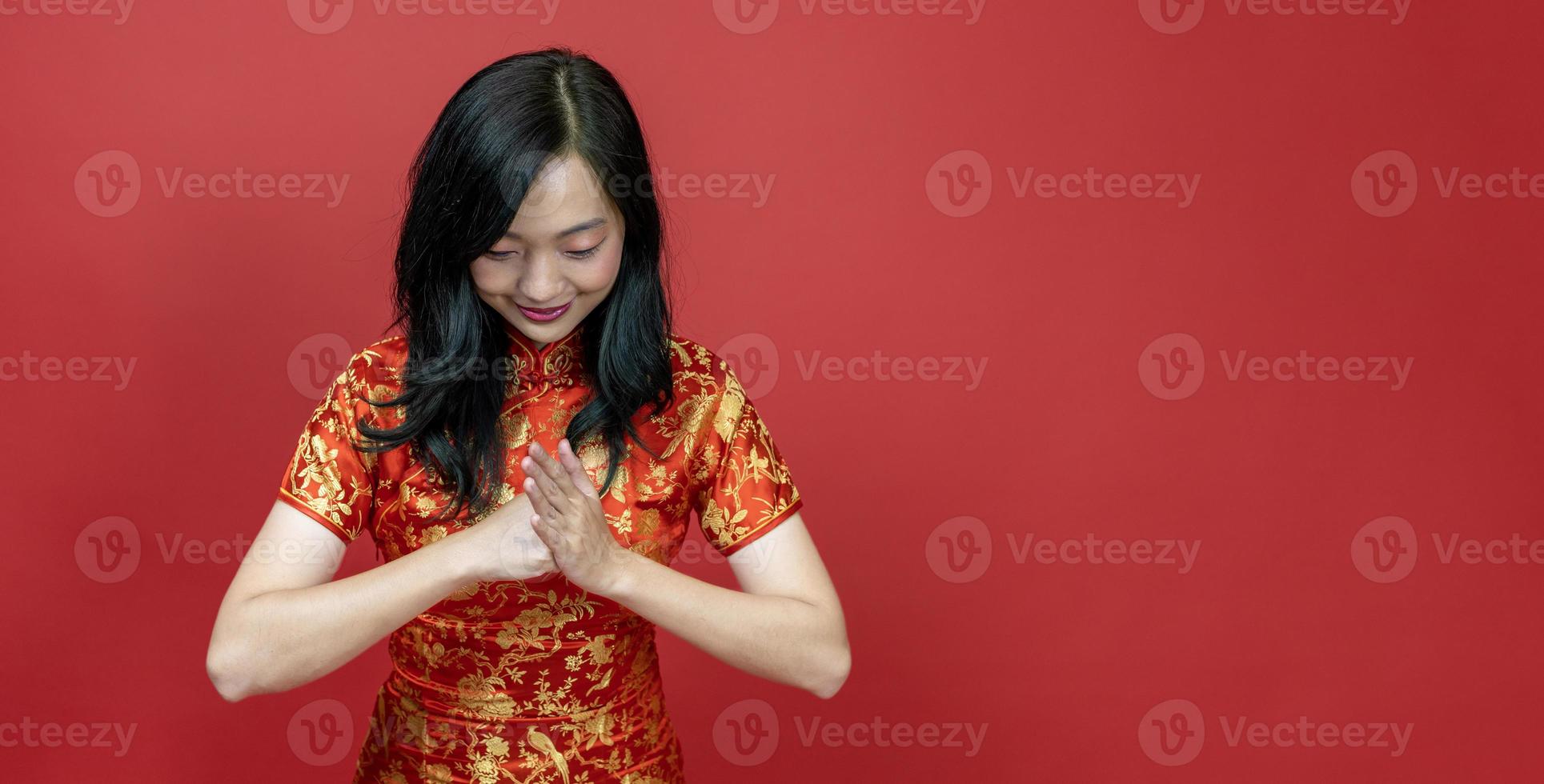 mulher chinesa asiática com cheongsam vermelho ou qipao fazendo gesto educado e respeitoso para desejar boa sorte e prosperidade no feriado de celebração do ano novo chinês isolado em fundo vermelho foto