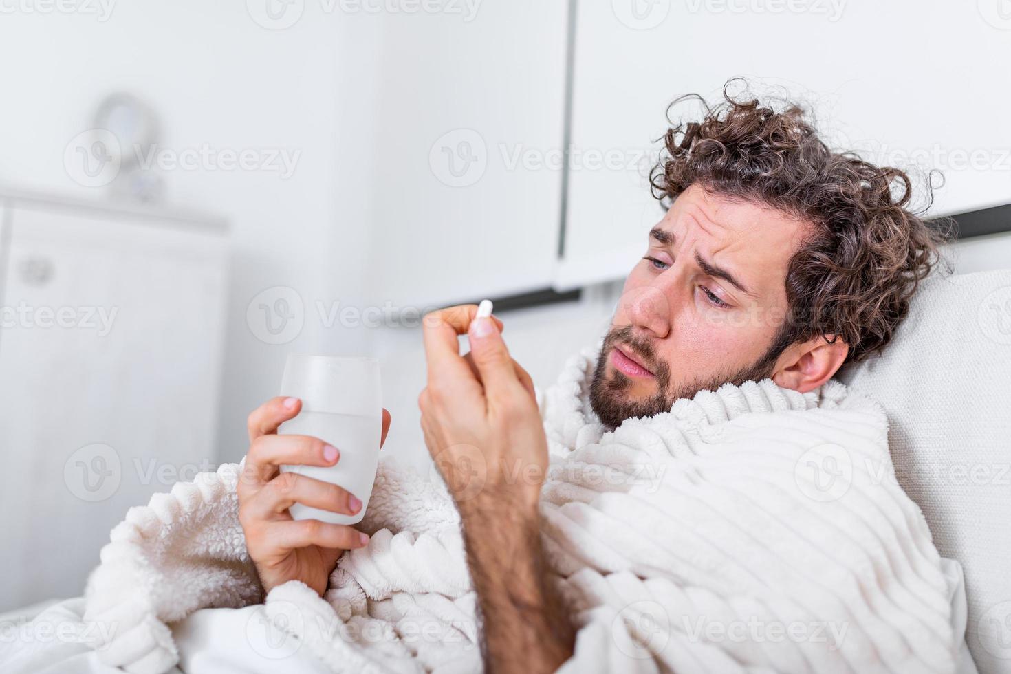 homem desperdiçado doente deitado na cama vestindo pijama sofrendo resfriado e vírus da gripe de inverno com comprimidos de remédio no conceito de cuidados de saúde bebendo pílulas com copo de água foto