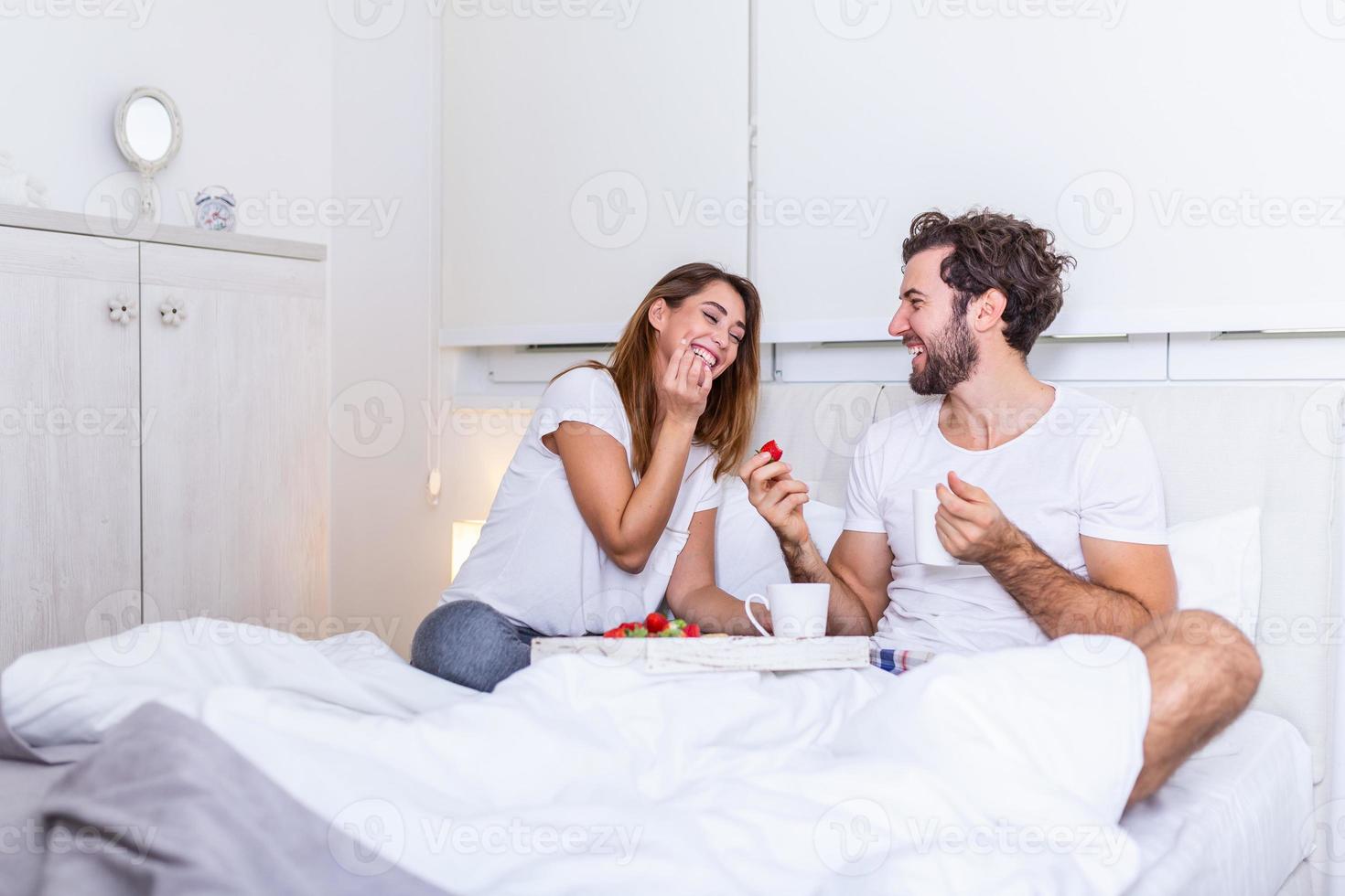 jovem bonito alimentando jovem atraente na cama pela manhã. café da manhã romântico para dois. amor, cuidado, relacionamentos. casal tomando café da manhã saudável juntos na cama em casa foto