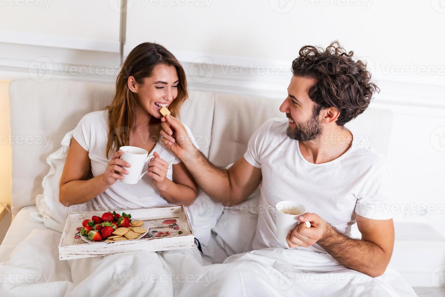 jovem bonito alimentando jovem atraente na cama pela manhã. café da manhã romântico para dois. amor, cuidado, relacionamentos. casal tomando café da manhã saudável juntos na cama em casa foto