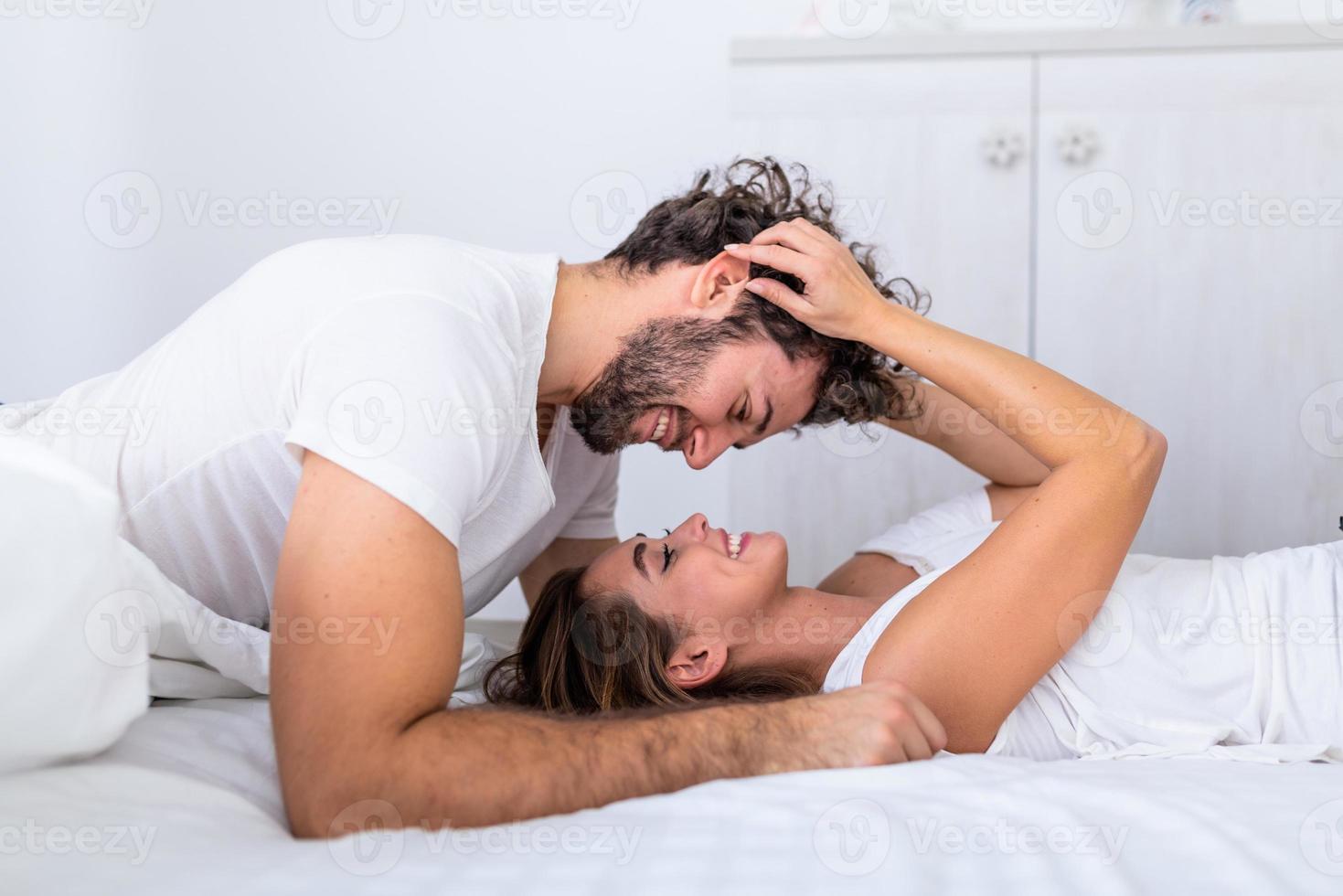 casal atraente jovem carinhoso compartilhando um momento romântico no quarto em casa. casal jovem feliz abraçando e sorrindo enquanto estava deitado na cama em um quarto em casa. foto