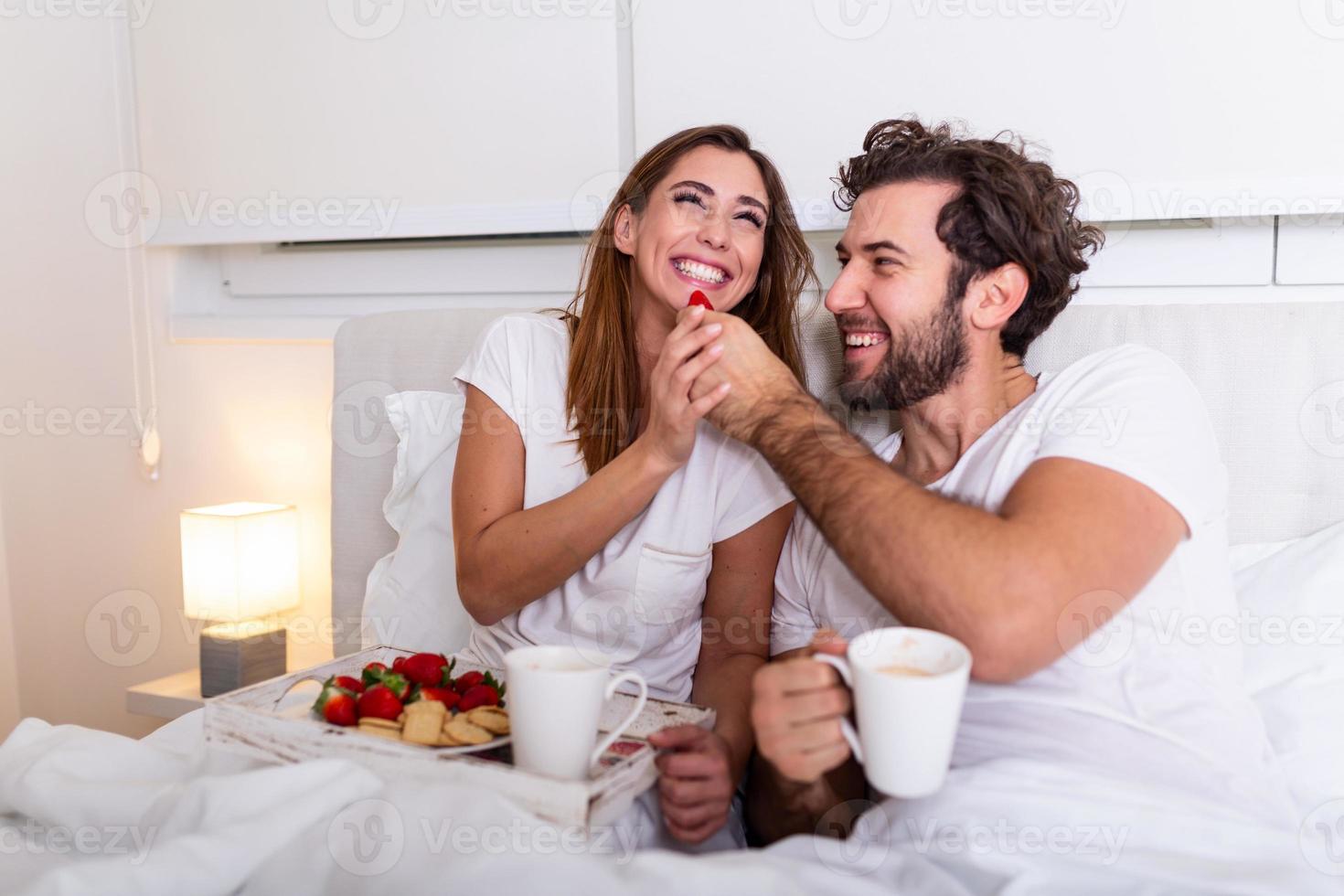 casal apaixonado tomando café da manhã na cama. jovem casal caucasiano tomando café da manhã romântico na cama. feminino e masculino, duas xícaras de café, frutas e biscoitos coloridos. foto