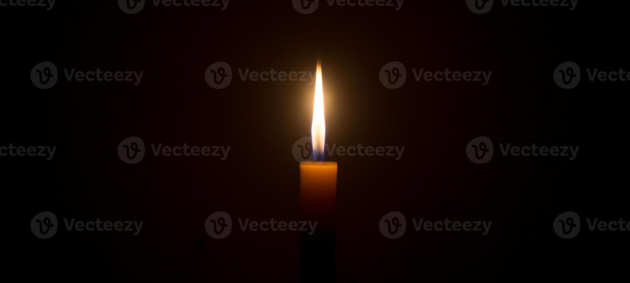 uma única chama de vela acesa ou luz brilhando em uma vela branca em fundo preto ou escuro na mesa na igreja para o natal, funeral ou serviço memorial foto