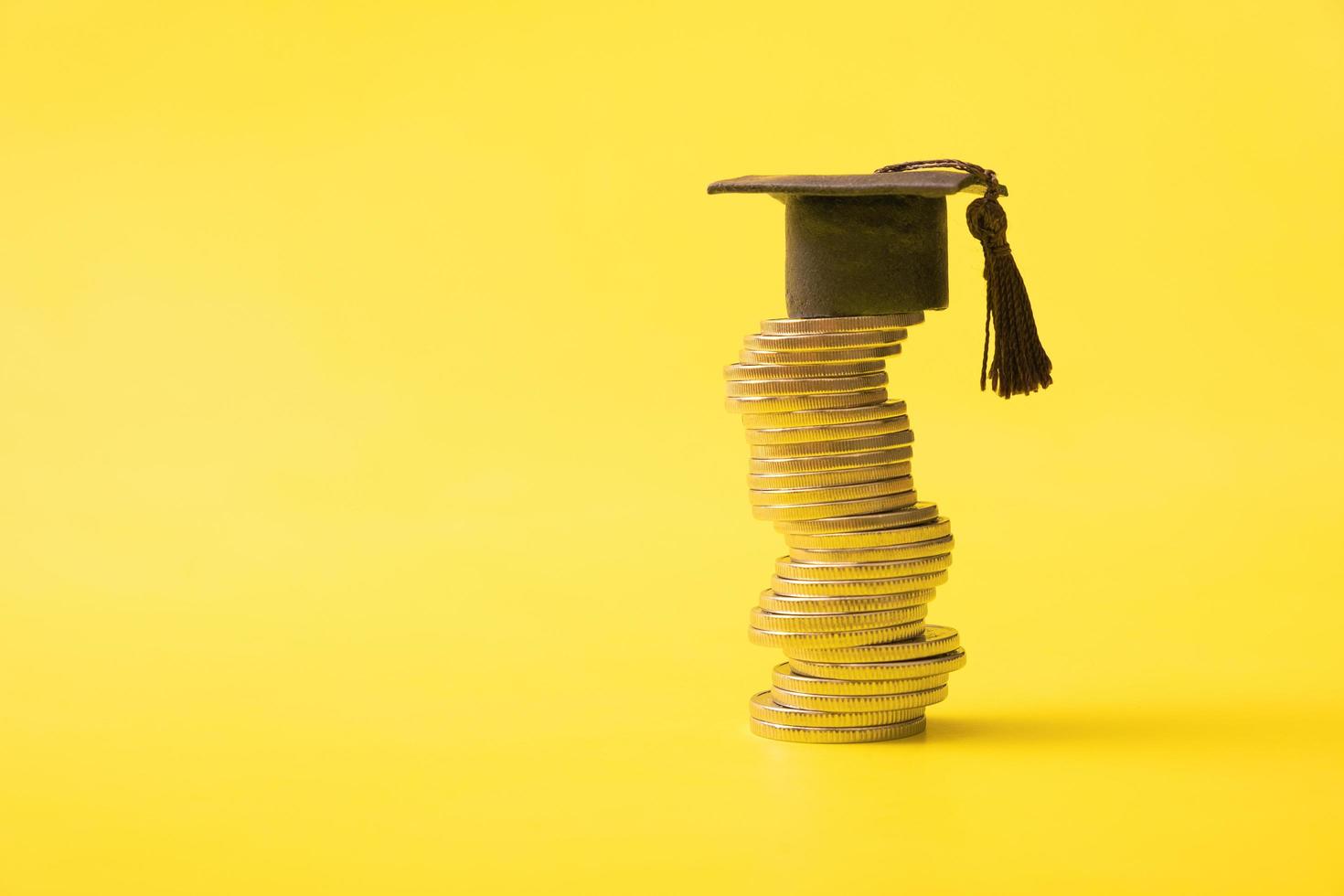 boné graduado com moedas em fundo amarelo. poupança para o conceito de educação. copie o espaço foto