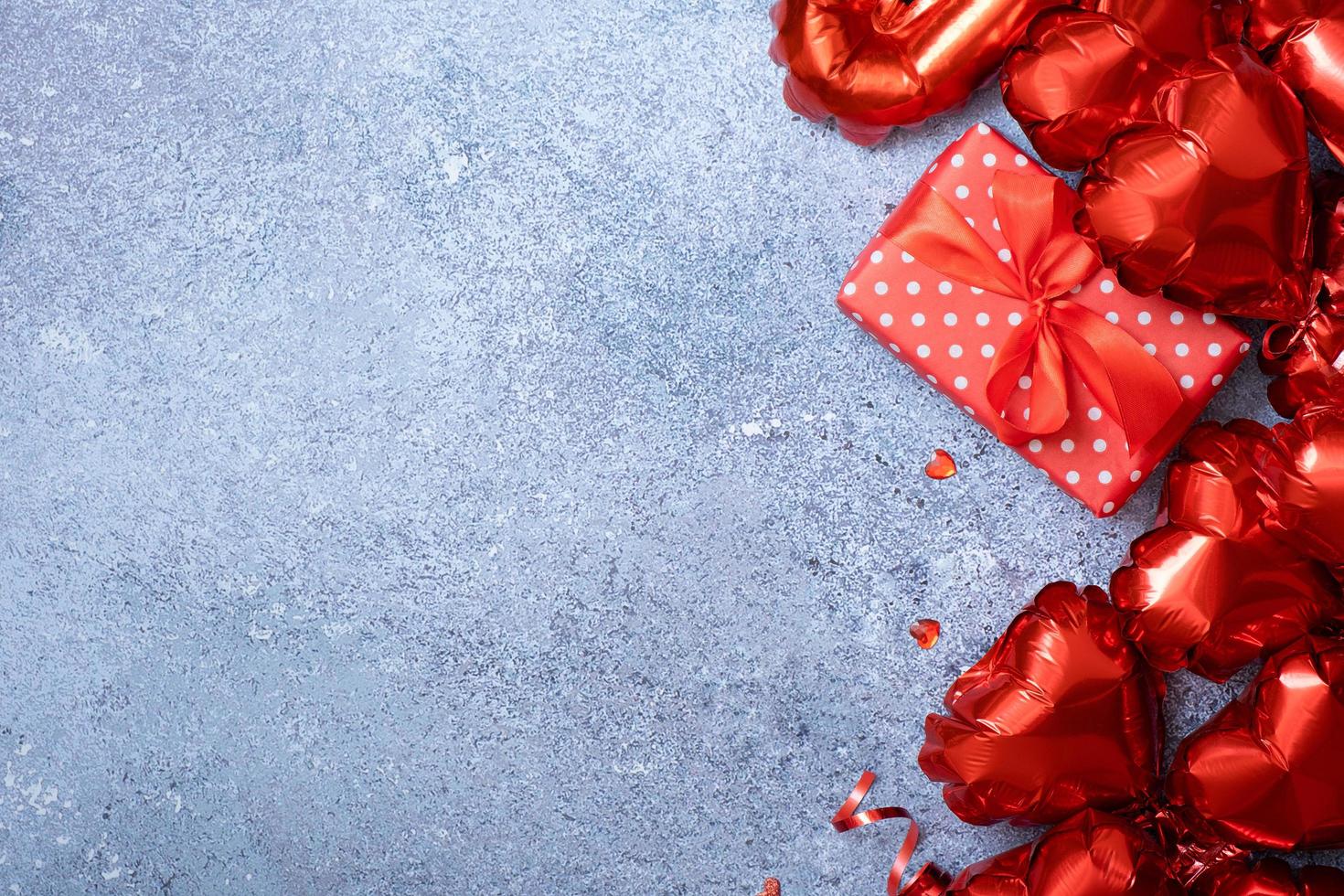 balões de forma de coração vermelho e caixa de presente em fundo de concreto. modelo de cartão de dia dos namorados. copie o espaço foto
