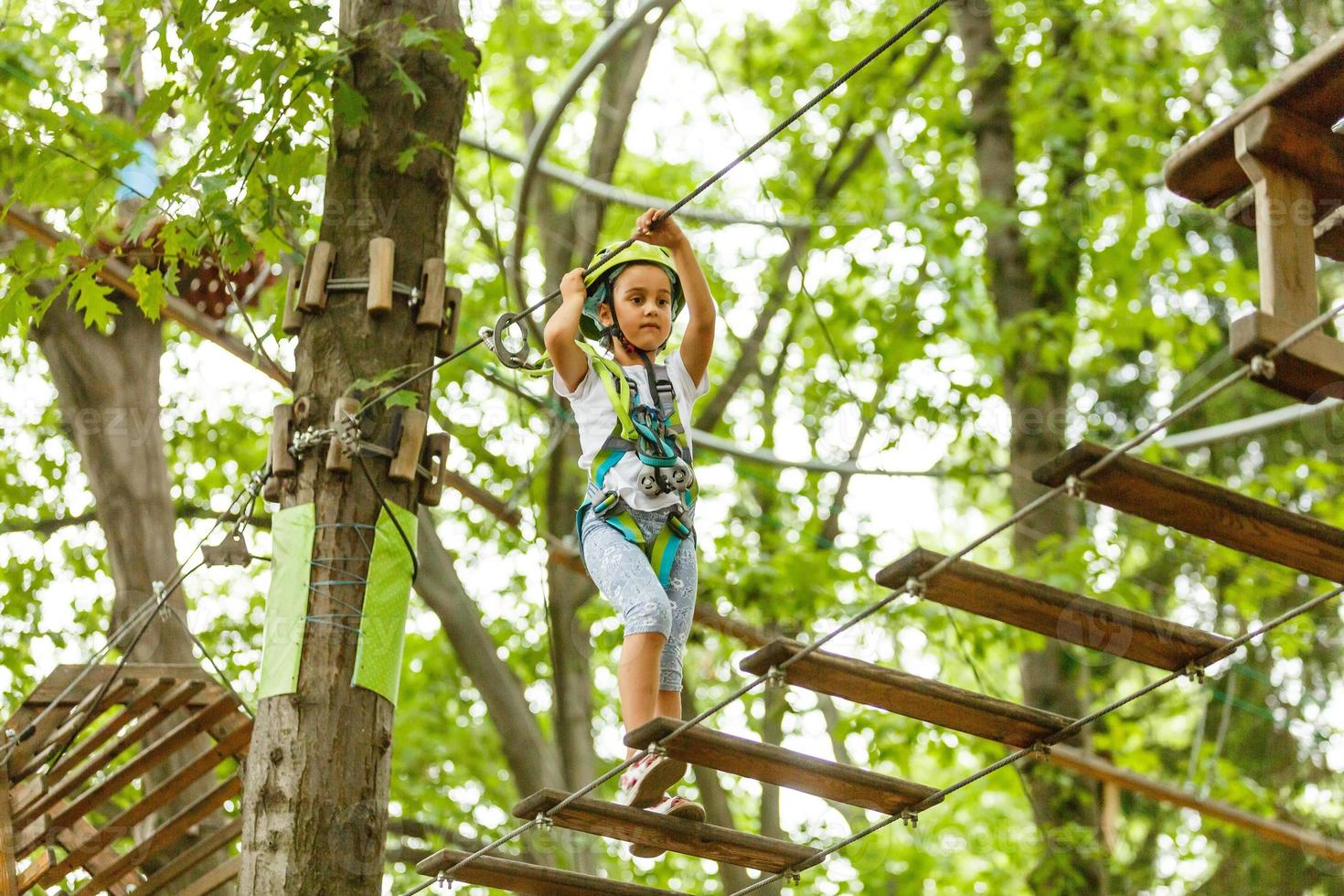 adorável menina aproveitando seu tempo na escalada do parque de aventura em um dia quente e ensolarado de verão. atividades de verão para crianças pequenas. criança se divertindo nas férias escolares. foto