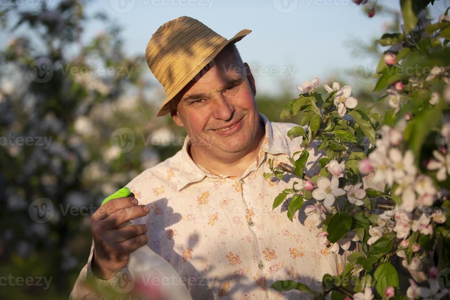 um homem idoso com um chapéu de palha em um jardim florido com um pulverizador. foto