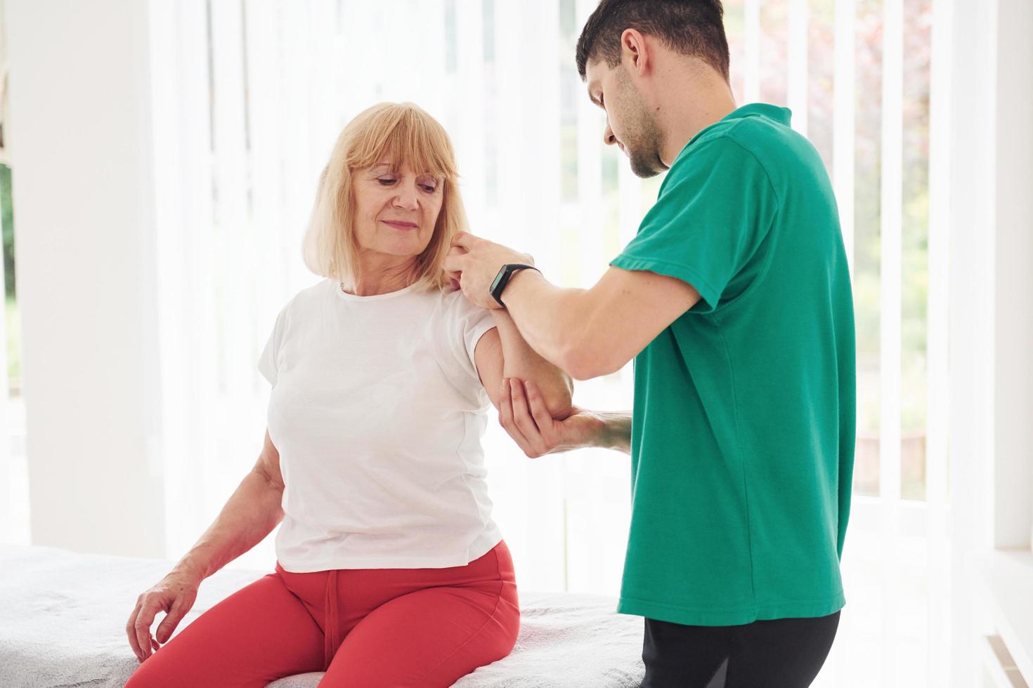 mulher mais velha tem uma visita na clínica e tem reabilitação. instrutor masculino ajudando-a foto