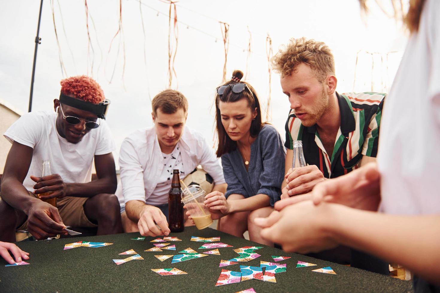 jogo de cartas. grupo de jovens em roupas casuais faz uma festa no telhado juntos durante o dia foto