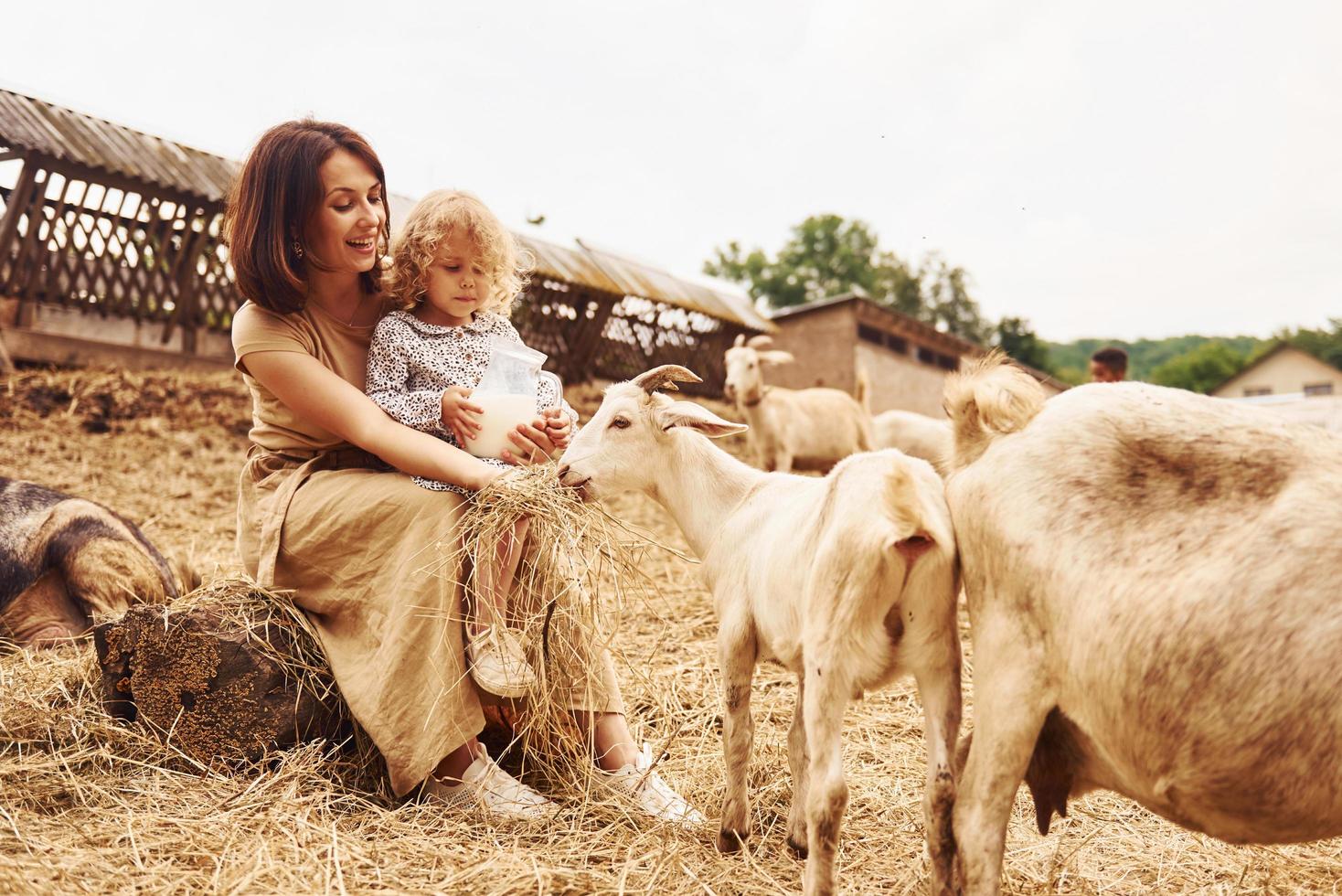 jovem mãe com sua filha está na fazenda no verão com cabras foto