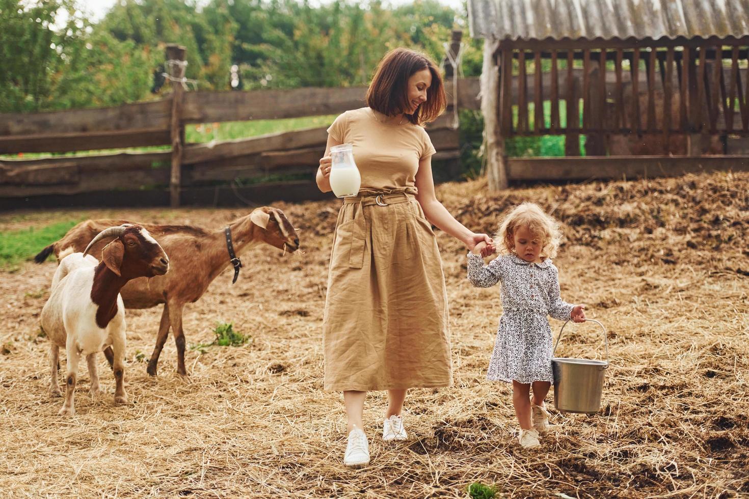 leite natural fresco. jovem mãe com sua filha está na fazenda no verão com cabras foto