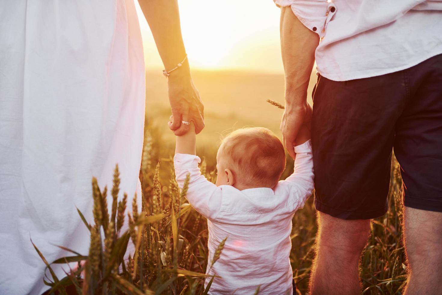 mãe e pai com seu filho passando o tempo livre no campo em dia ensolarado de verão. vista de trás foto