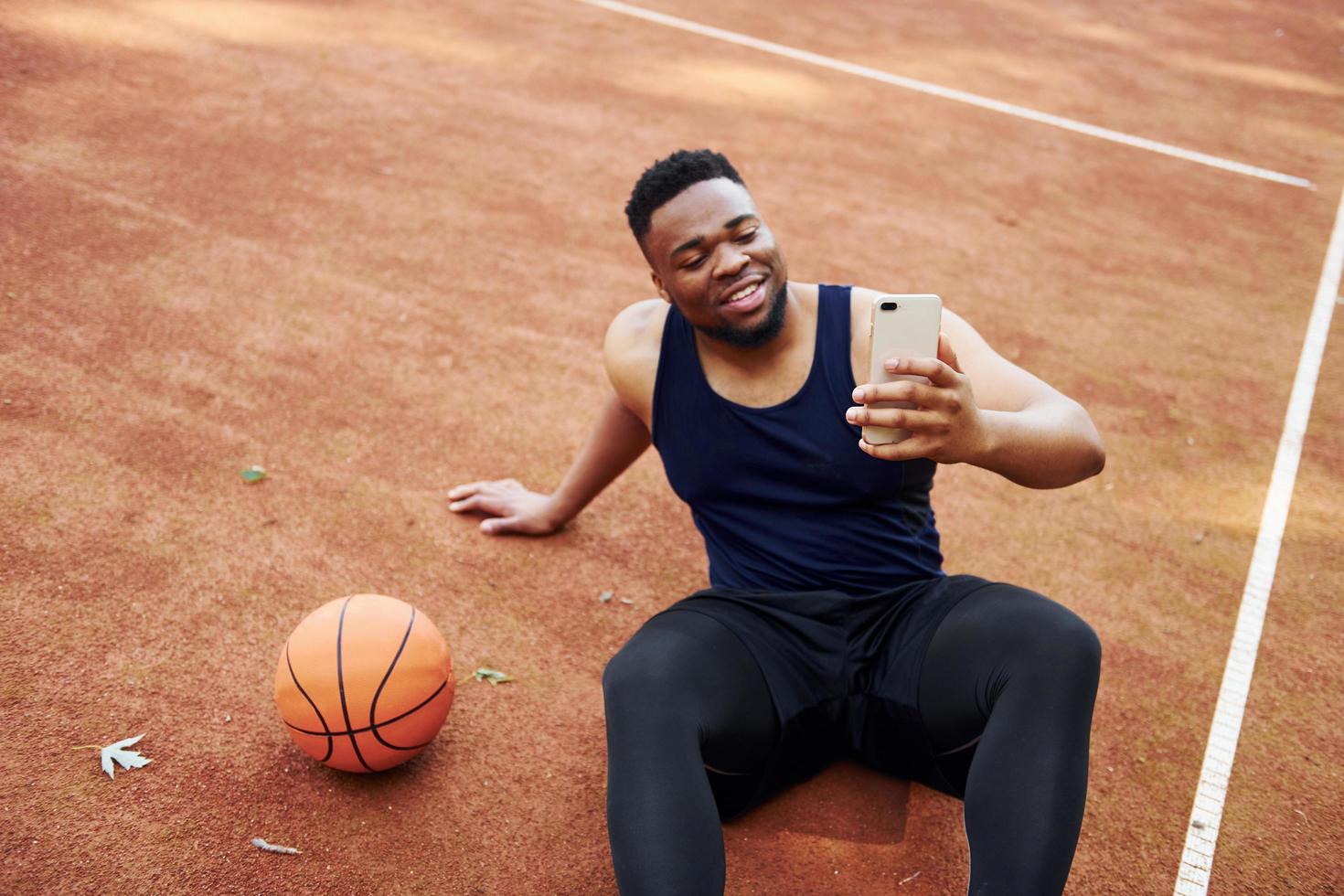 fazendo selfie. homem afro-americano joga basquete na quadra ao ar livre foto