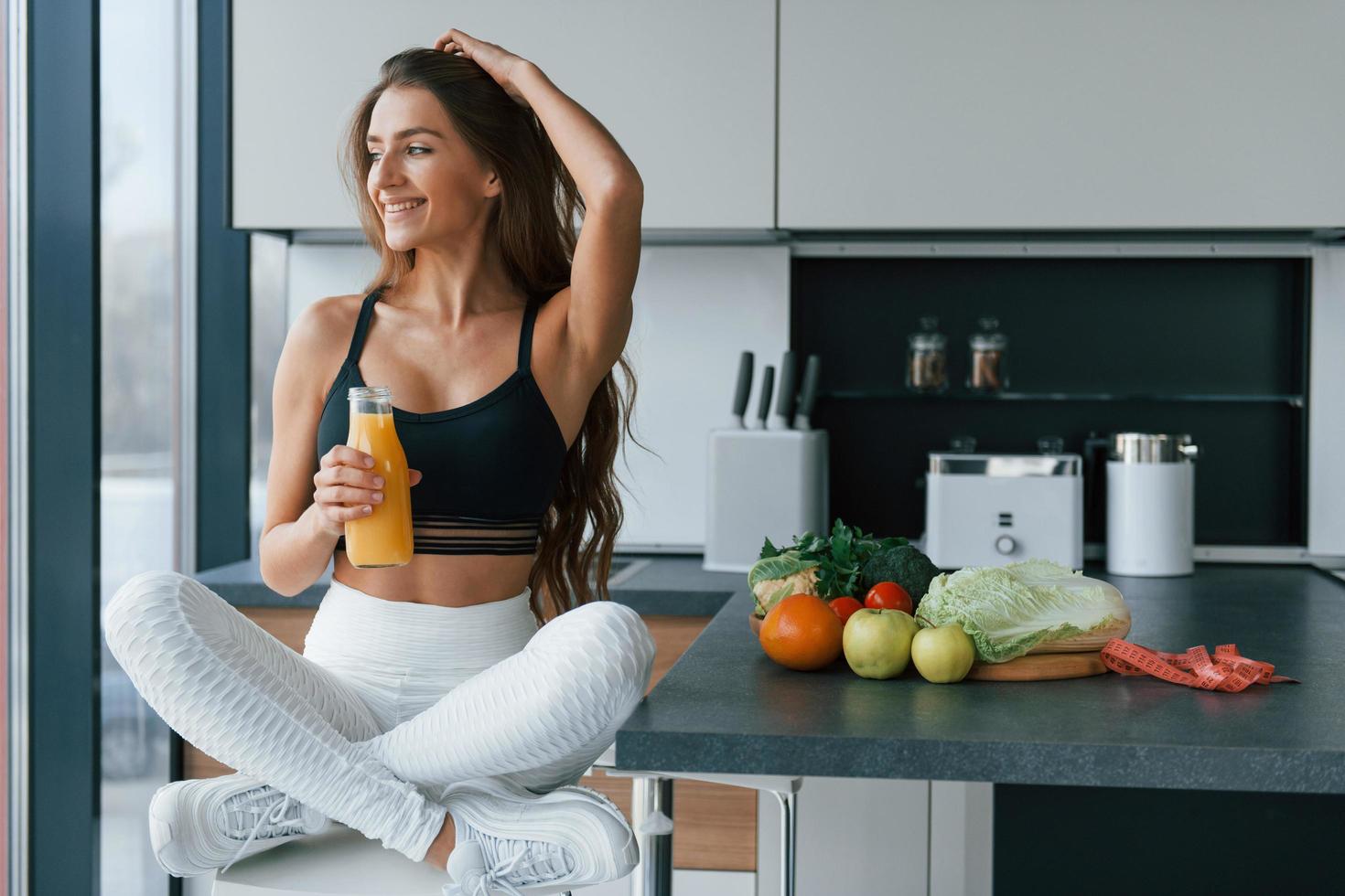 com suco de laranja fresco. jovem europeia está dentro de casa na cozinha dentro de casa com comida saudável foto