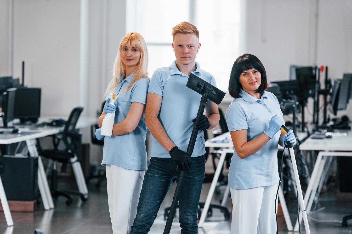 cara com aspirador de pó. grupo de trabalhadores limpa escritório moderno juntos durante o dia foto