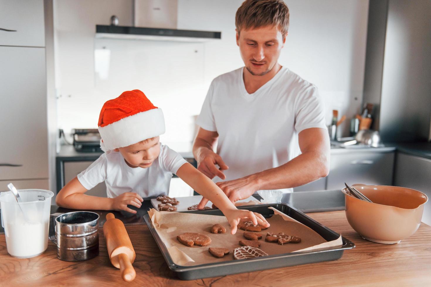 de pé ao lado da mesa. pai ensinando seu filho pequeno a preparar biscoitos doces de natal foto