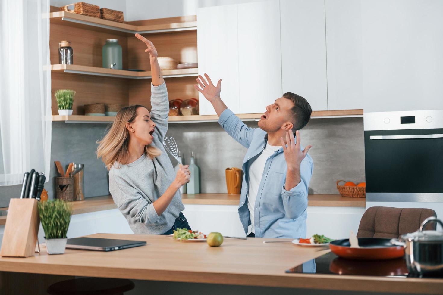 se divertindo. casal preparando comida em casa na cozinha moderna foto