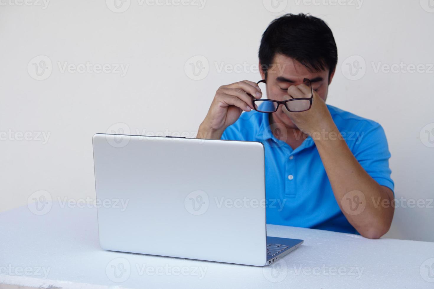 homem asiático, sente os olhos feridos, segura os óculos durante o trabalho no laptop. conceito, problema de visão. optometria. óculos com lentes convexas ou côncavas. miopia.doença ocular foto