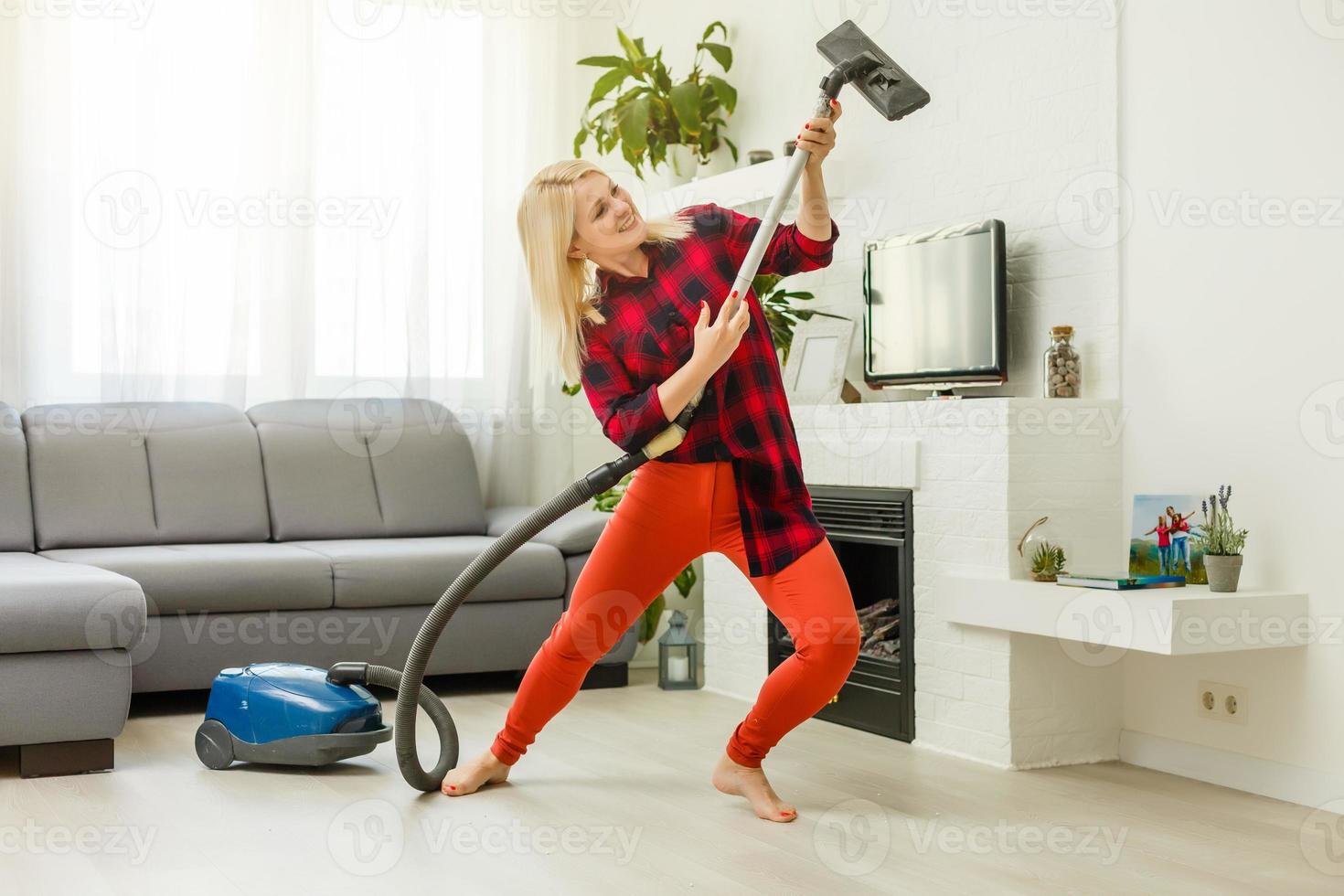 sorrindo animada jovem dona de casa se divertindo enquanto limpava o chão com aspirador de pó. mulher feliz fazendo tarefas domésticas em casa gosta de música usando fones de ouvido. foto