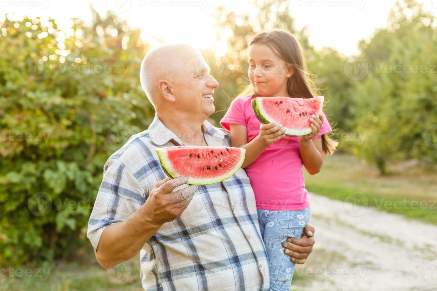 avô e neta comem melancia e riem no jardim na grama no verão foto