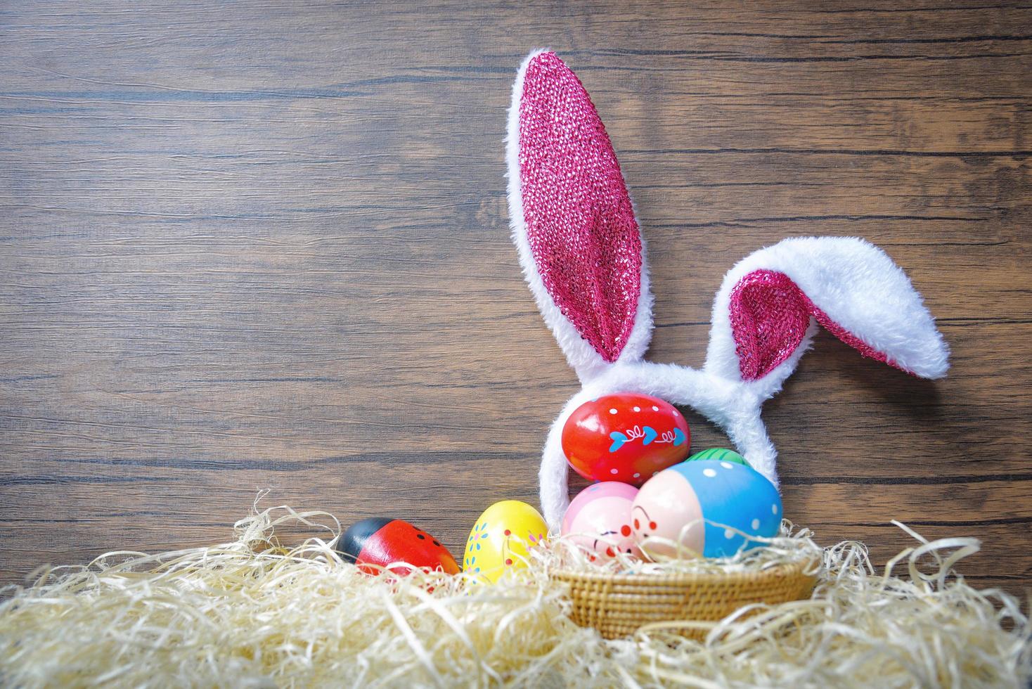 ovos de páscoa coloridos e coelho de orelha de coelhinho da páscoa na decoração de ninho de cesta e fundo de madeira foto