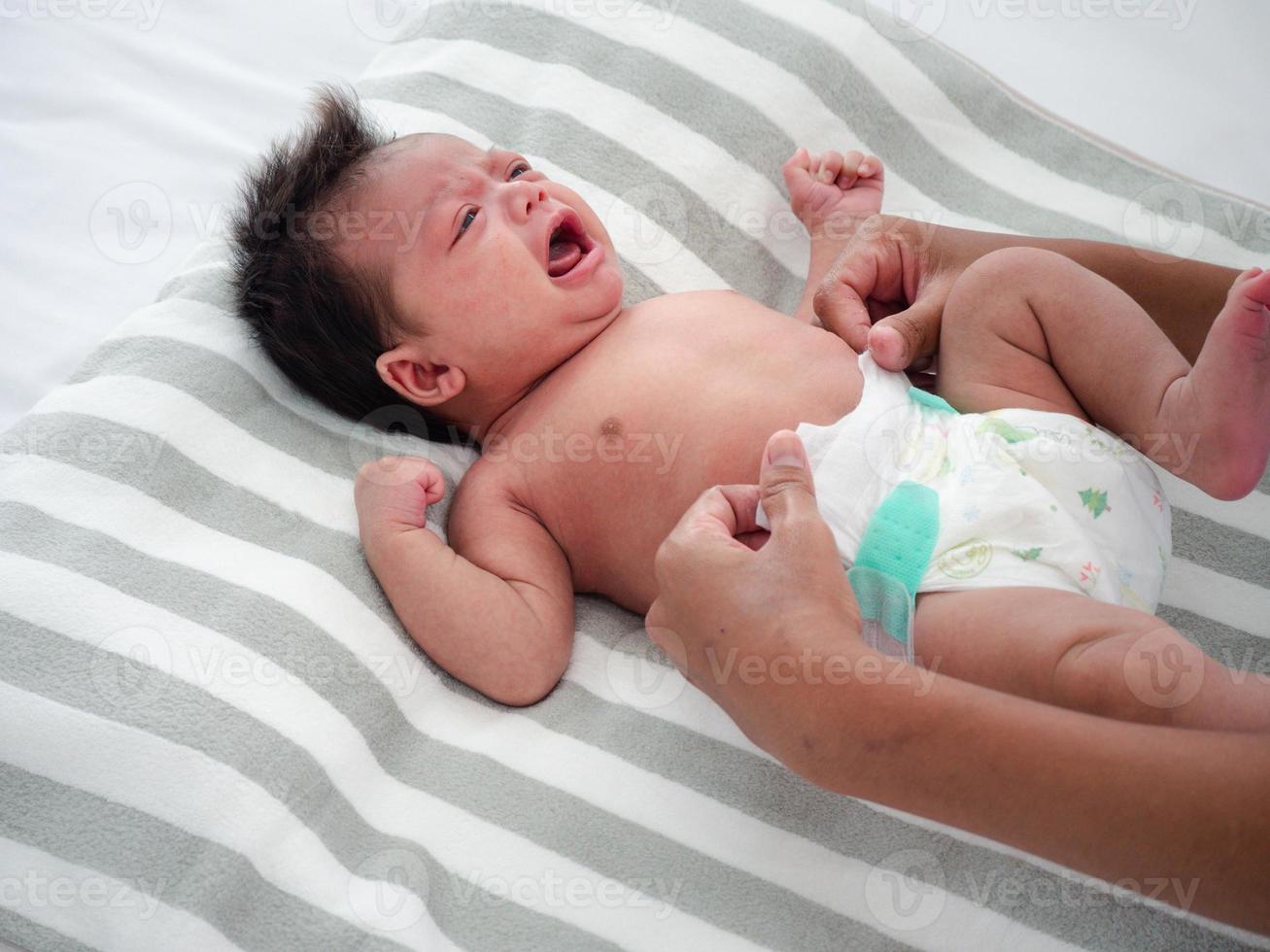 menina bonita chorando enquanto a mãe trocava a fralda. bebê asiático-australiano de raça mista veste-se após o banho de sua mãe. conceito de cuidados de saúde. foto