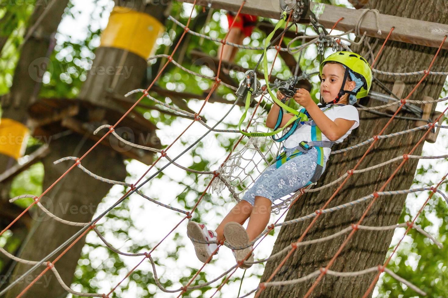 adorável menina aproveitando seu tempo na escalada do parque de aventura em um dia quente e ensolarado de verão. atividades de verão para crianças pequenas. criança se divertindo nas férias escolares. foto