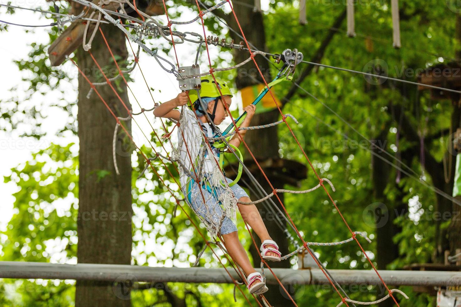 adorável menina aproveitando seu tempo na escalada do parque de aventura em um dia quente e ensolarado de verão. atividades de verão para crianças pequenas. criança se divertindo nas férias escolares. foto