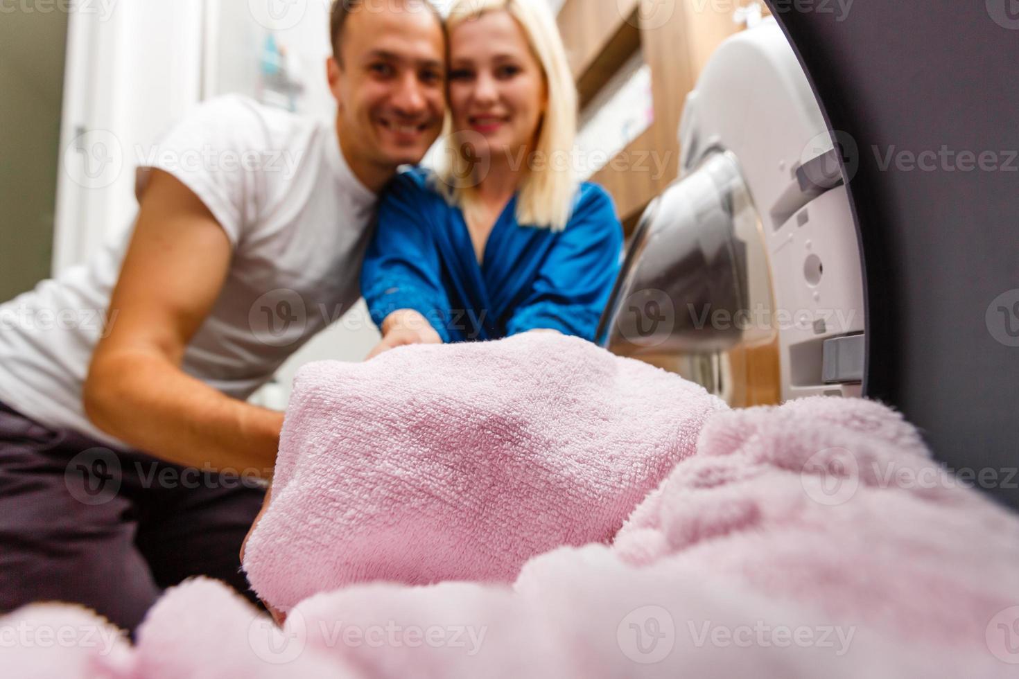 casal engraçado carregando roupas para máquina de lavar foto