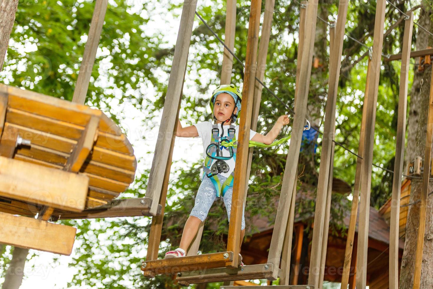 menina da escola feliz desfrutando de atividade em um parque de aventura escalada num dia de verão foto