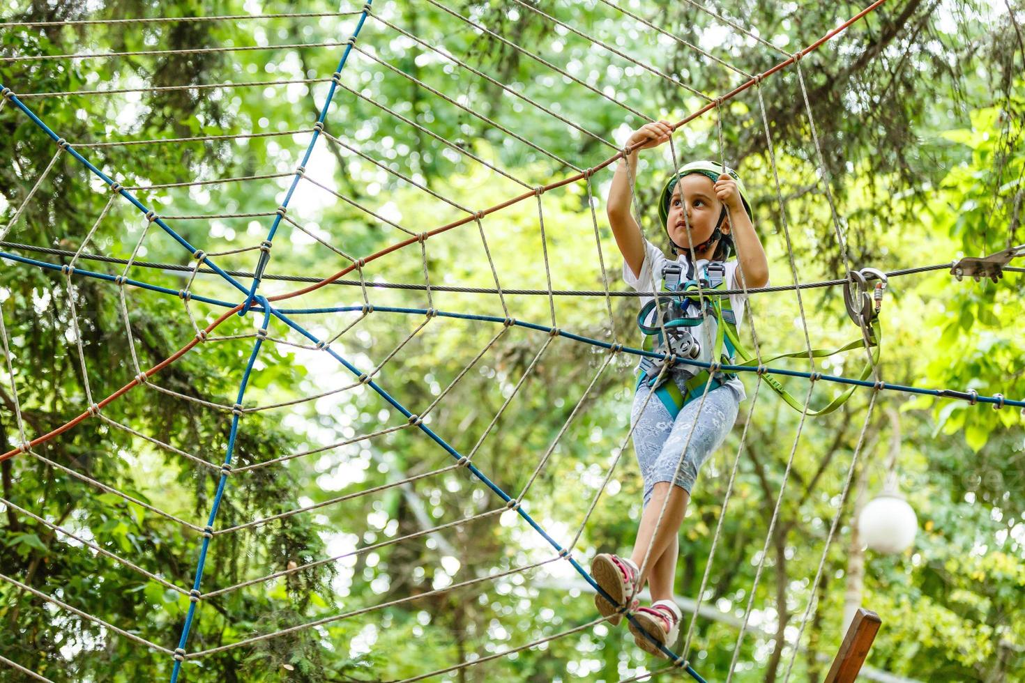 menina adorável aproveitando seu tempo no parque de aventura de escalada em um dia quente e ensolarado de verão foto