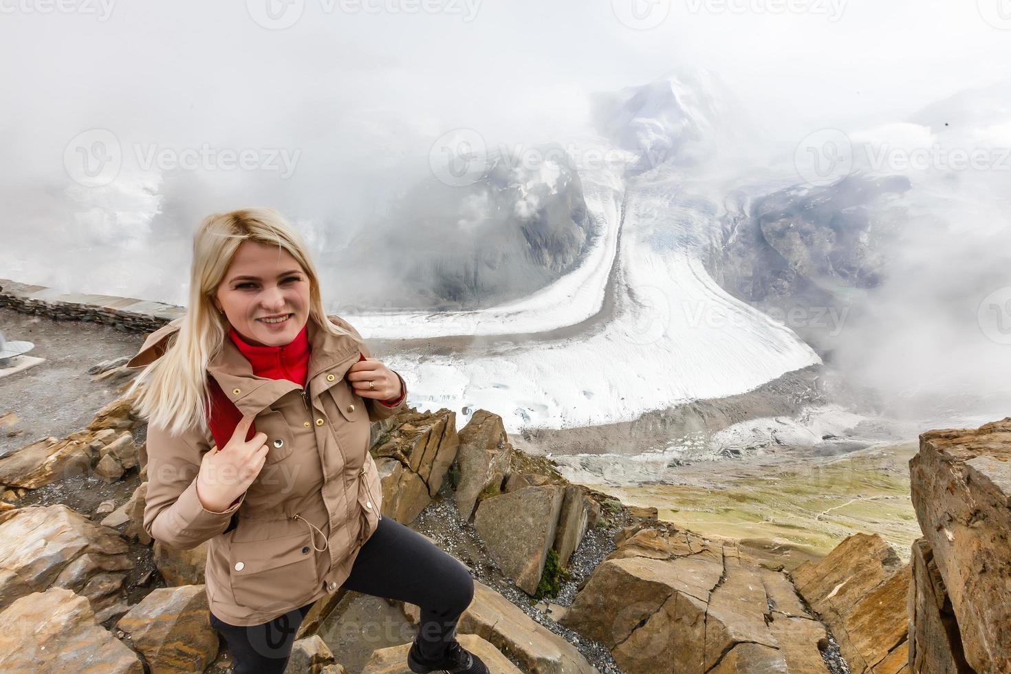 jovem mulher feliz com mochila em pé sobre uma rocha e olhando para um vale abaixo foto