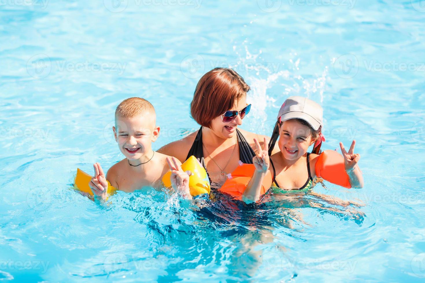 bela jovem mãe com filho e filha na piscina. foto