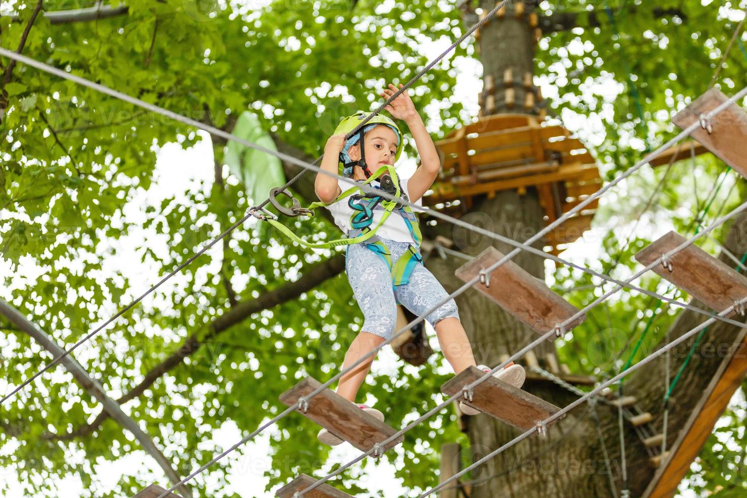 menina da escola feliz desfrutando de atividade em um parque de aventura escalada num dia de verão foto