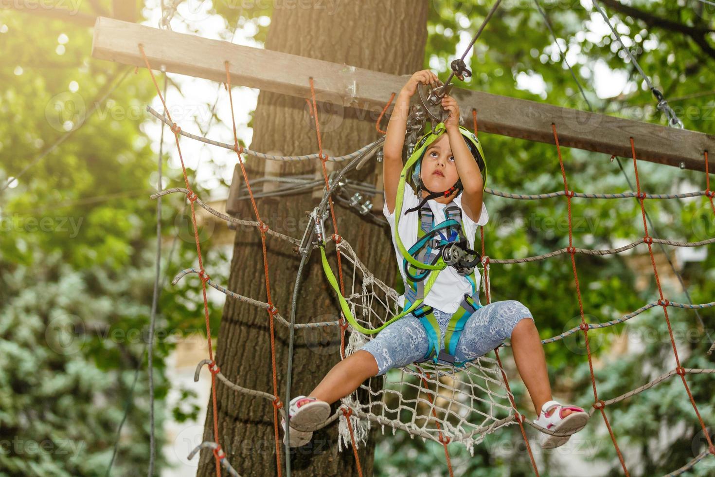 adorável menina aproveitando seu tempo na escalada do parque de aventura em um dia quente e ensolarado de verão. atividades de verão para crianças pequenas. criança se divertindo nas férias escolares. foto