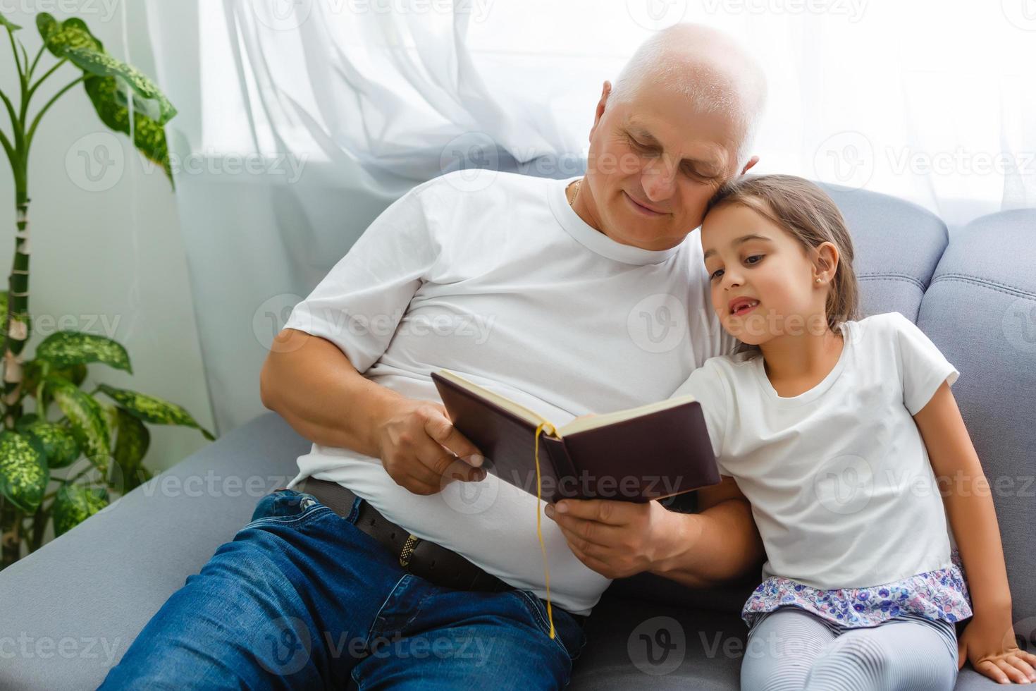 menina feliz com avô lendo livro de histórias em casa foto