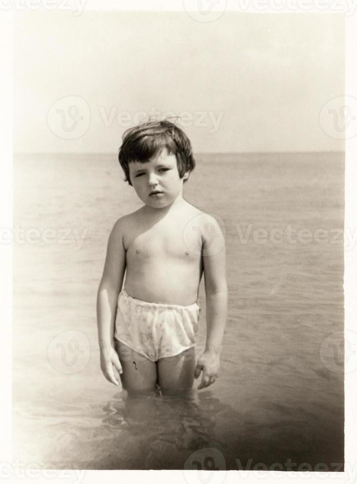 uma criança, uma menina de maiô na água à beira-mar em uma foto de família. costa do mar negro da crimeia por volta de 1972.