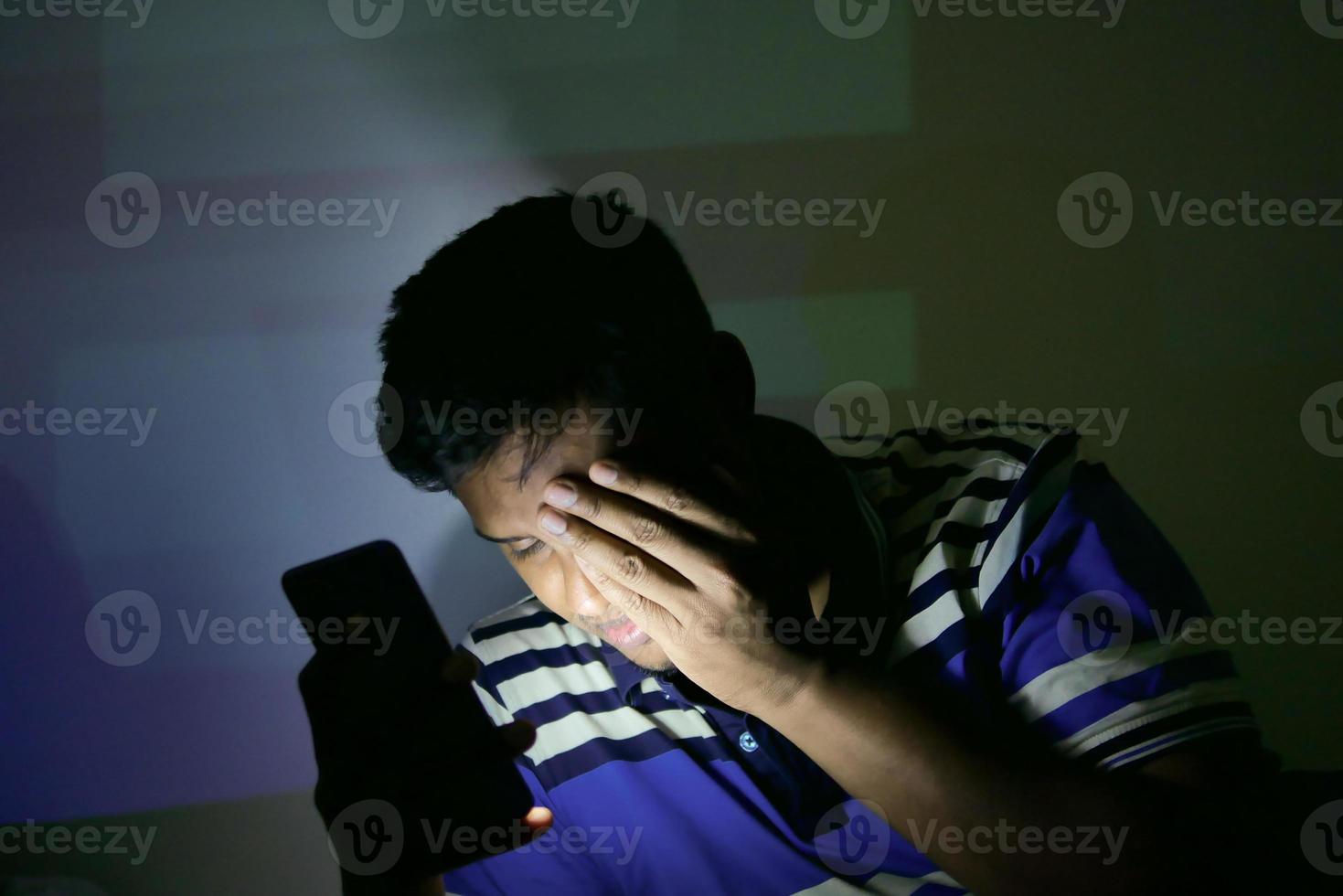 jovem na cama usando telefone inteligente à noite sofrendo de dor nos olhos foto