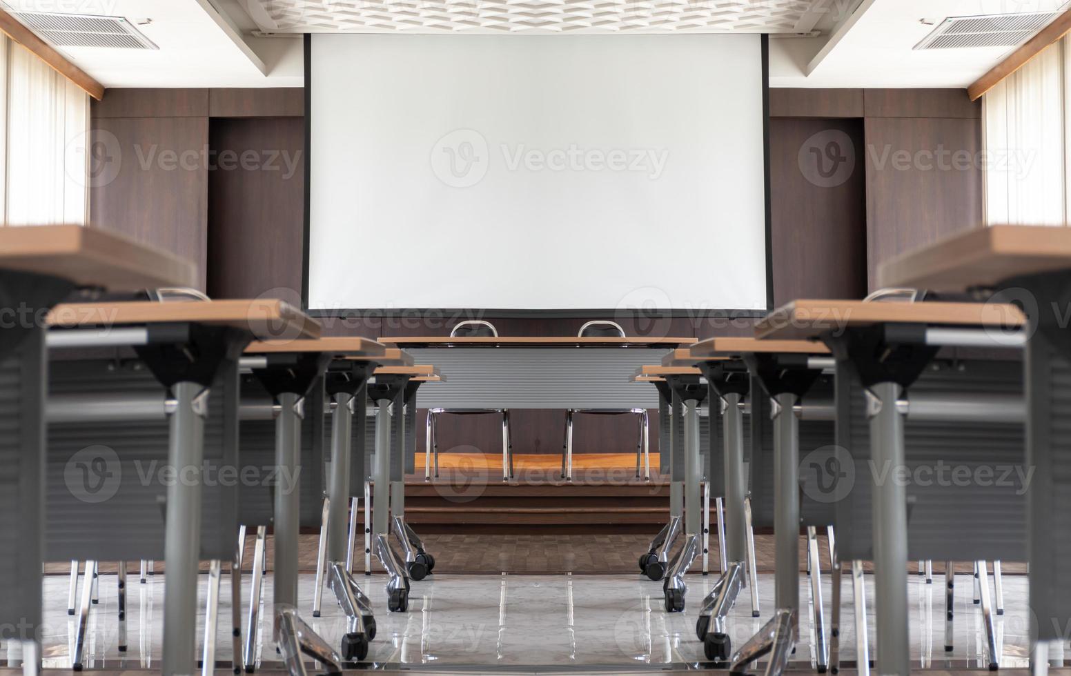sala de seminários com uma mesa de alto-falante no meio do palco e fundo de tela branca foto